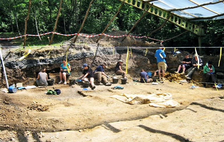 Researchers sit on the dirt at the dig site where they found the Rudapithecus fossil