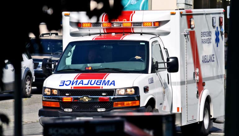 A mostly-white ambulance drives down the street with its lights on