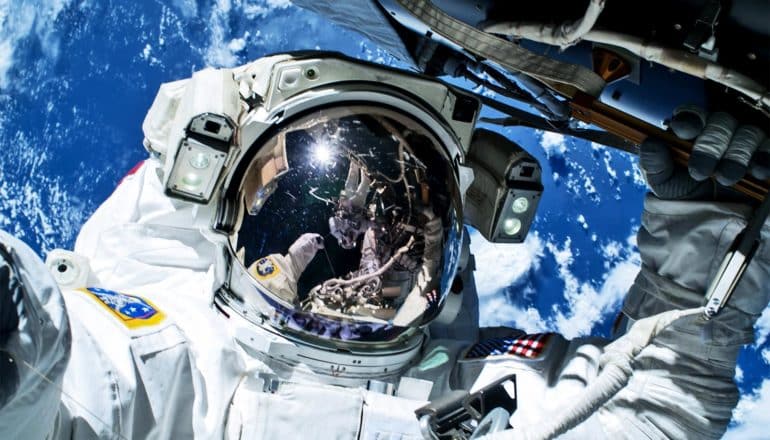 An astronaut takes a selfie during a space walk, with the Earth glowing blue in the background