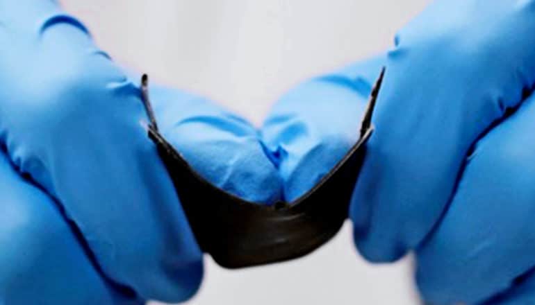 A researcher with blue gloves on bends the battery at its center