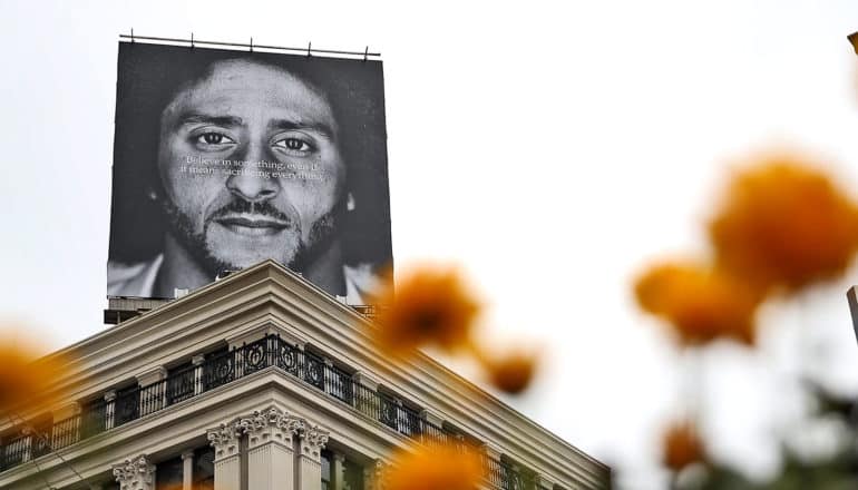 Billboard atop building says Believe in something. Even if it means sacrificing everything." over Colin Kaerpnick's face. Blurry orange flowers in foreground