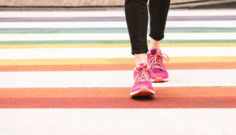 lower legs of person in hot pink sneakers in rainbow-painted crosswalk