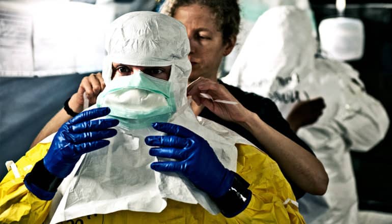 An health worker gets suited up during an Ebola recovery effort, getting help to tie on a protective mask from another worker