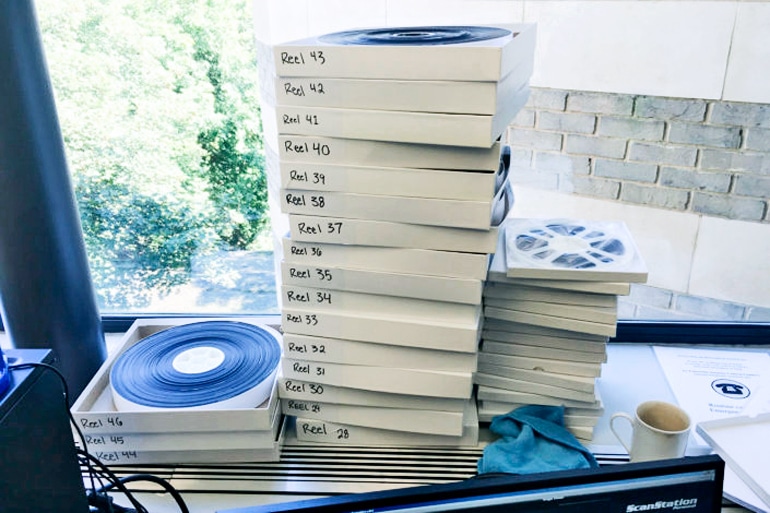 A series of film reels in boxes sit on top of each other in several tall stacks, against a window