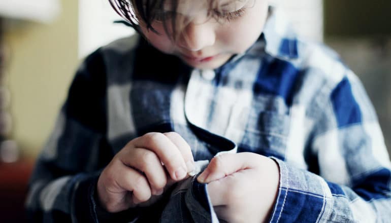 young child tries to button flannel shirt