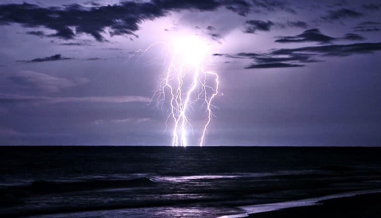 Lightning strikes over the ocean, turning the dark night sky a deep shade of purple