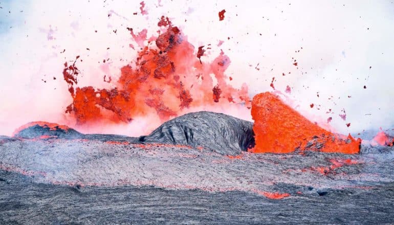 A volcano erupts, with solid magma in the foreground and bright orange liquid lava bursting from the ground beyond