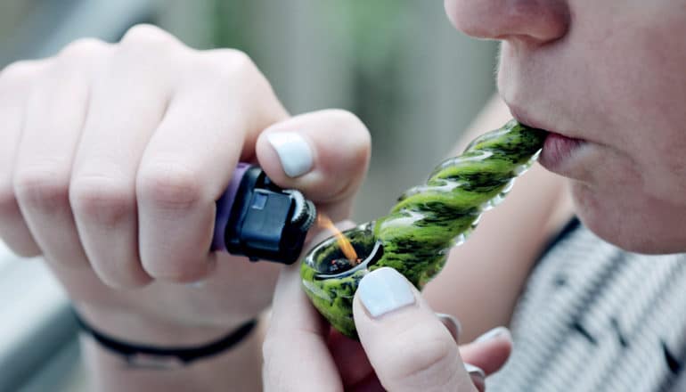 person lights green glass bowl with lighter to smoke marijuana