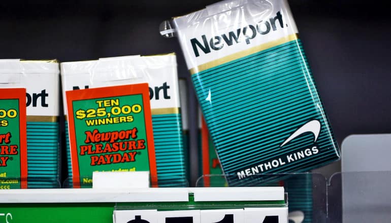 A few packs of menthol cigarettes sit on a shelf at the store, with one pack almost coming off the shelf