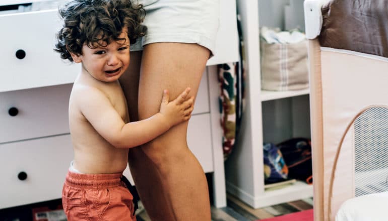 crying toddler clings to mother's legs