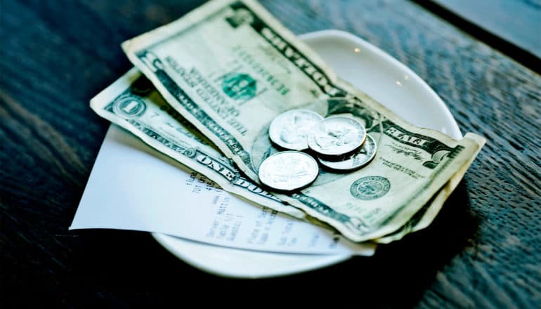 Money sits on top of the receipt on a small dish on a restaurant table