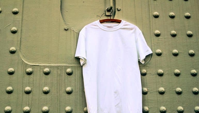 white t-shirt on hanger against green metal wall with rivets