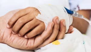 A parent holds a child's bandaged hand, which has an IV going into it