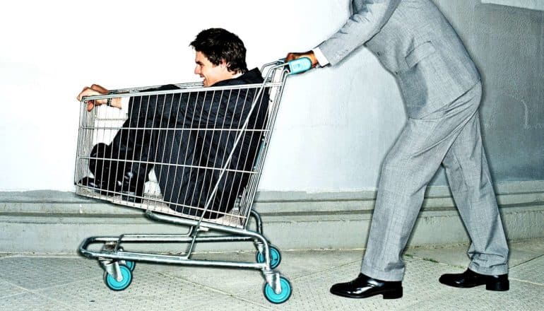 figure in suit pushes person in shopping cart