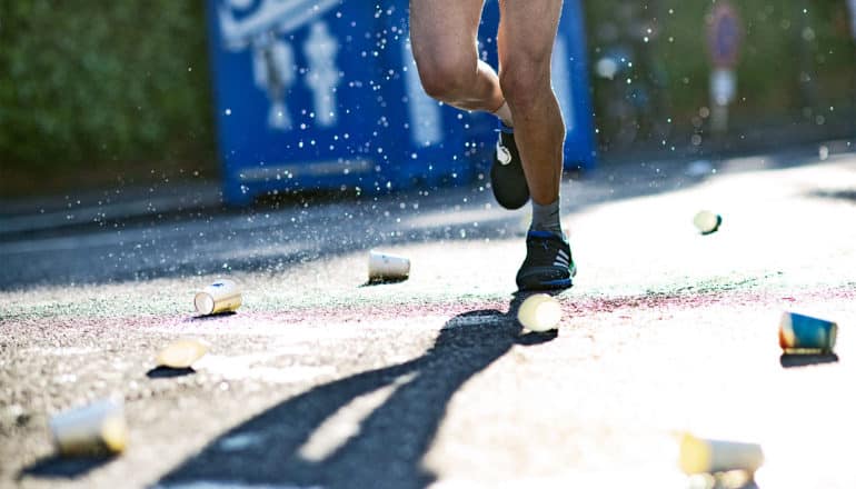 A marathon runner's legs are surrounded by empty paper water cups on the road