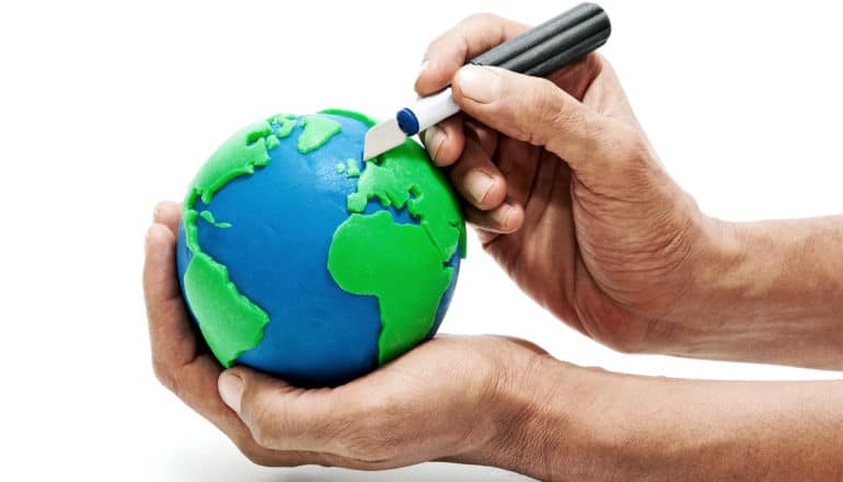 A man holds a clay globe, cutting away pieces with a sculpting knife