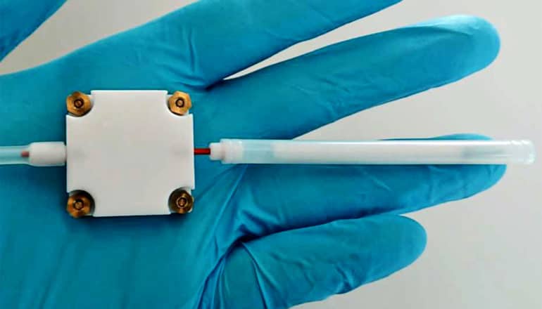 A blue glove holds the sensor device, a white square with a tube sticking out