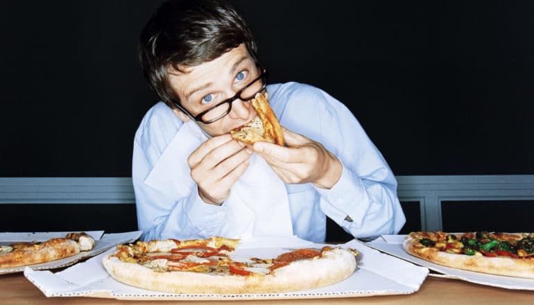 person looks up while eating a lot of pizza