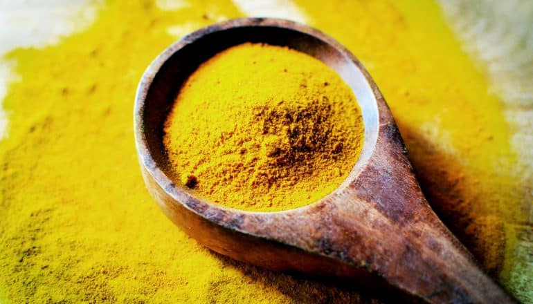 A wooden spoonful of turmeric sits on a pile of the spice