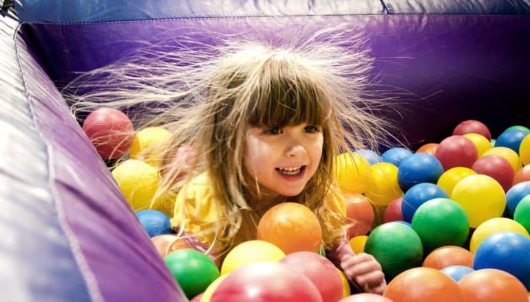 A young girl sits in a ball pit while her hair stands on end from static electricity