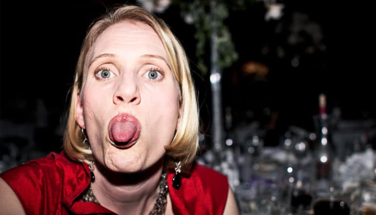 A woman in a red outfit turns to the camera from a table she's sitting at to stick her tongue out