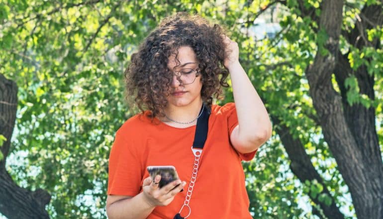 serious young person looks at phone while walking outdoors