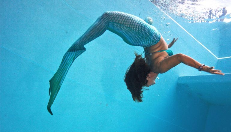 A swimmer is dressed like a mermaid, complete with long tail, as she moves upside-down underwater