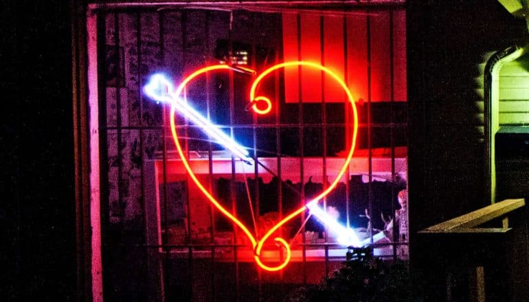 A tattoo shop's neon sign is in the shape of a heart with an arrow through it