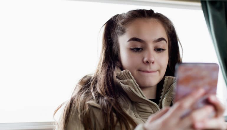 teenager uses phone in back of car