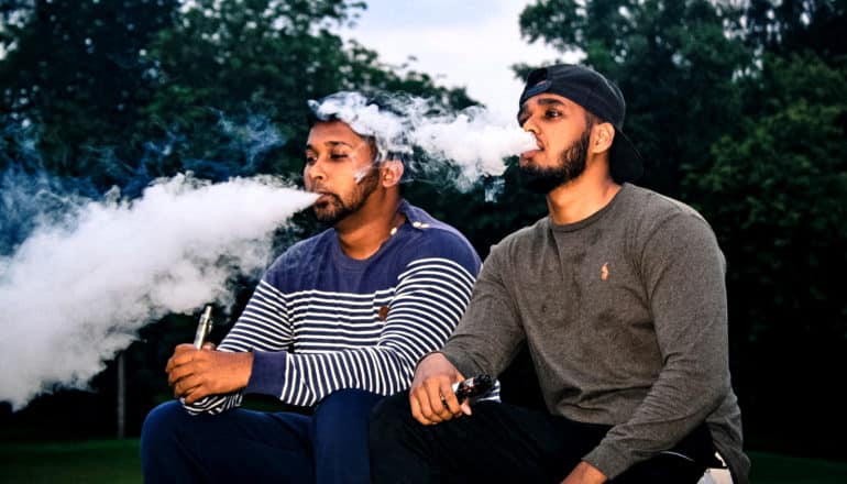 two people exhale vapor outdoors at dusk