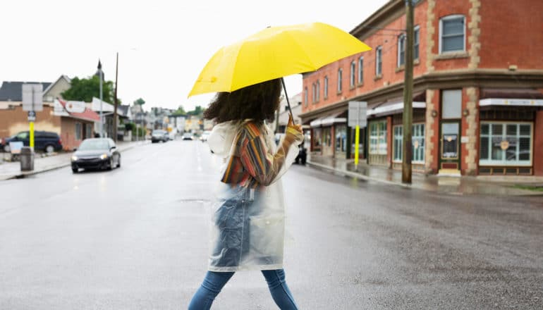 person in raincoat holding umbrella walks through intersection