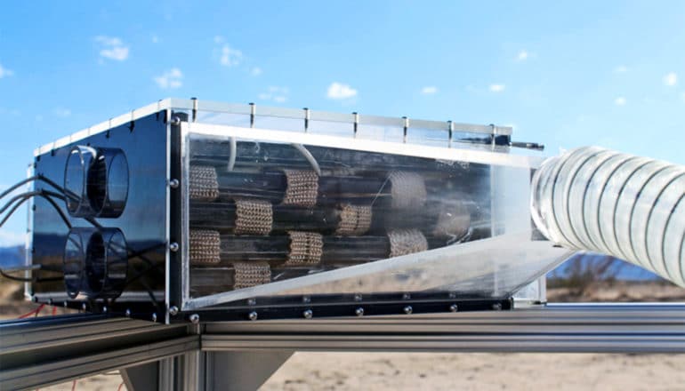 The small water harvester is a box with clear front and a tube running into it. Behind the box is a bright blue sky.
