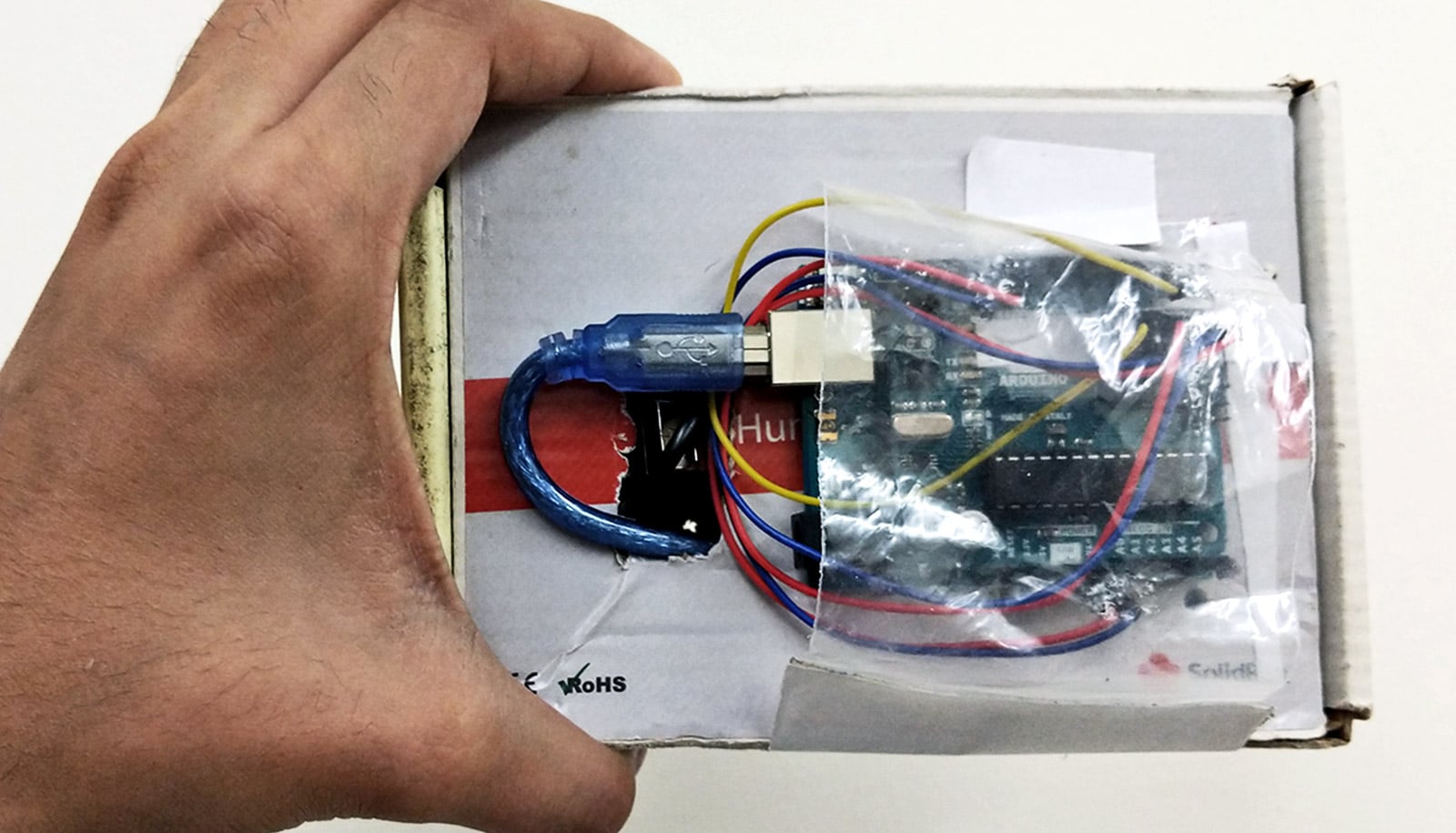 The device is a cardboard box with a USB cord coming out of it and into a chip covered in plastic