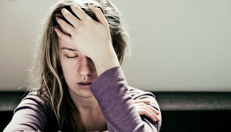 A woman in pain holds her hand to har head while her eyes are closed