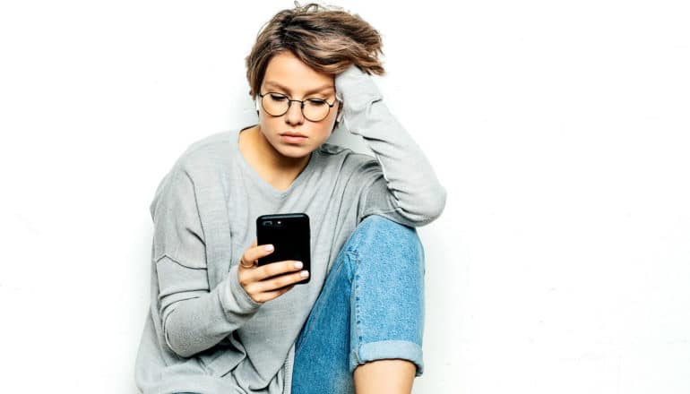 A woman with wireless earpods uses her phone against a white background