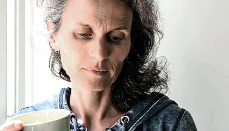 A woman holds a cup of coffee as she looks down with worry