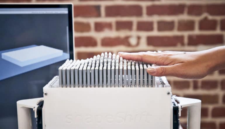 A person reaches out to touch the display, whic forms an image of what's on the screen