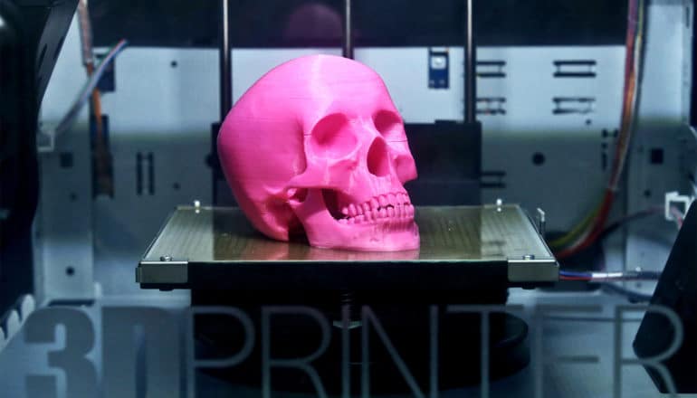 A pink 3D-printed skull sits inside a printer