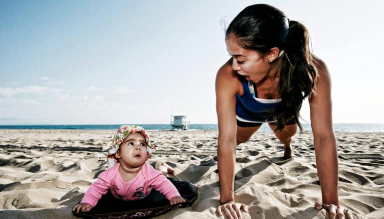 baby and mom make eye contact while doing "push ups" on the beach