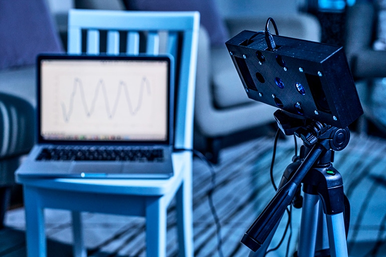 In a dark room, the smart speaker is connected to a laptop that shows a waveform 