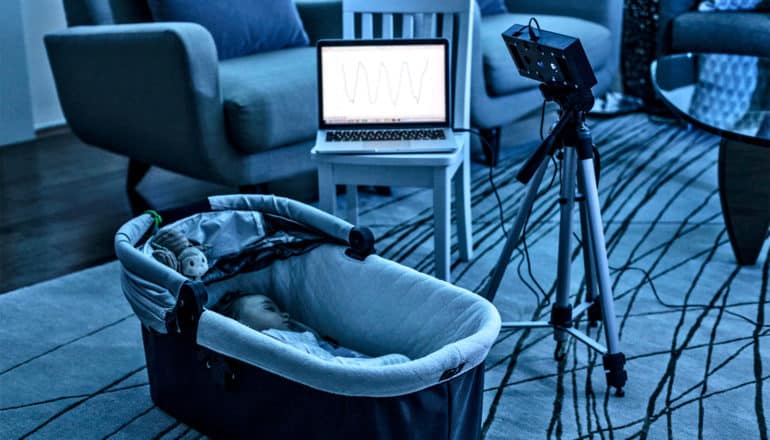 The BreathJunior system monitors a baby sleeping in a crib, with a speaker connected to a laptop