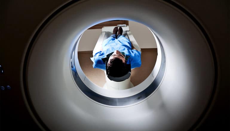 A person is about to get an MRI, as they lay down on a table in a blue hospital smock
