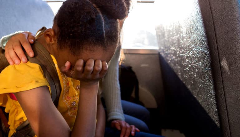 unseen friend puts arm around upset black child on school bus