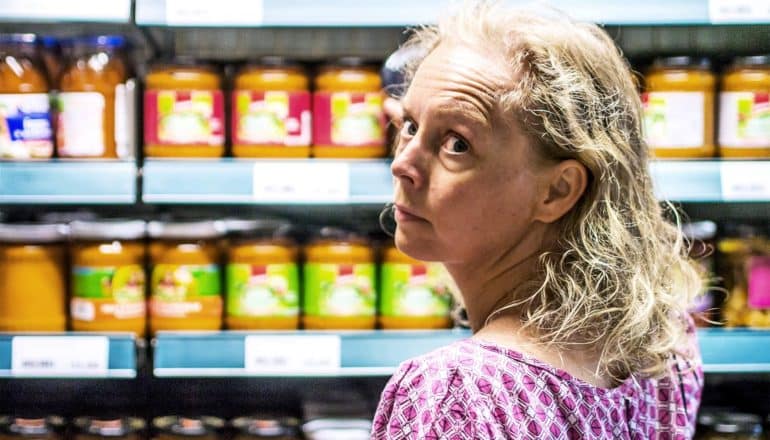 A woman looks away from the shelf in front of her towards the camera while standing in a supermarket aisle