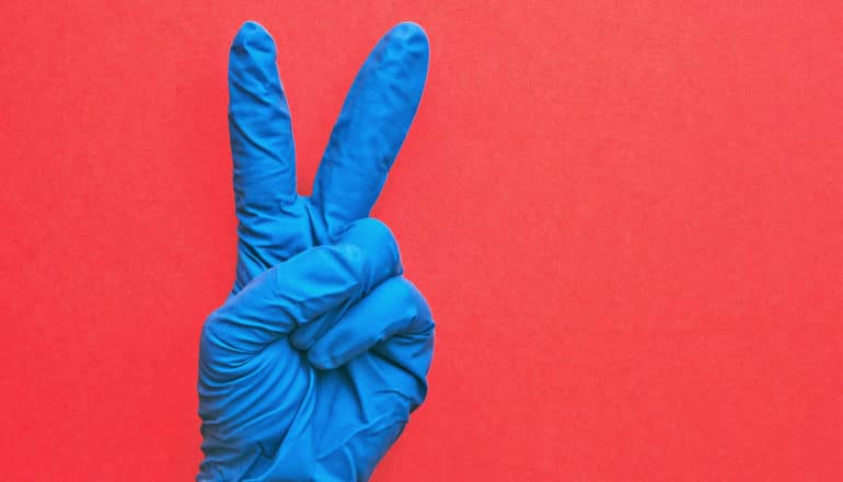 A blue gloved hand holds up two fingers against a red background