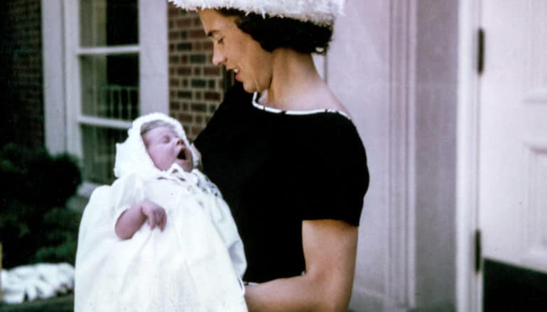 woman in 1950s or so holds baby in christening gown