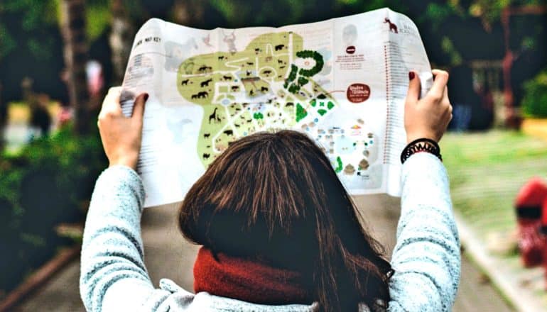 A young woman holds up a map with a path in the background