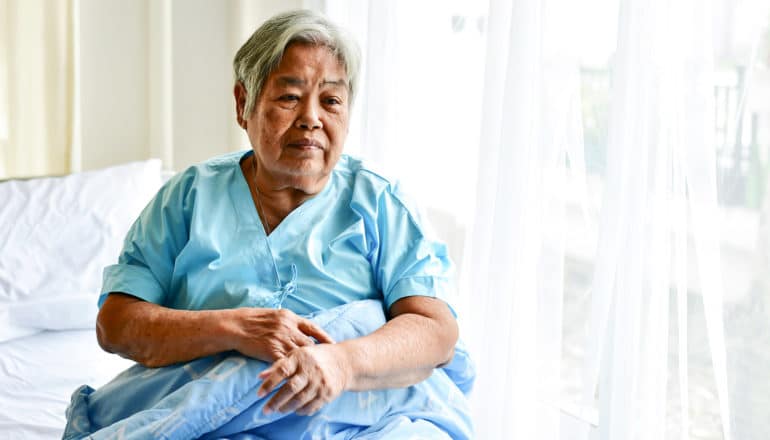An older woman sits in a hospital bed next to a window