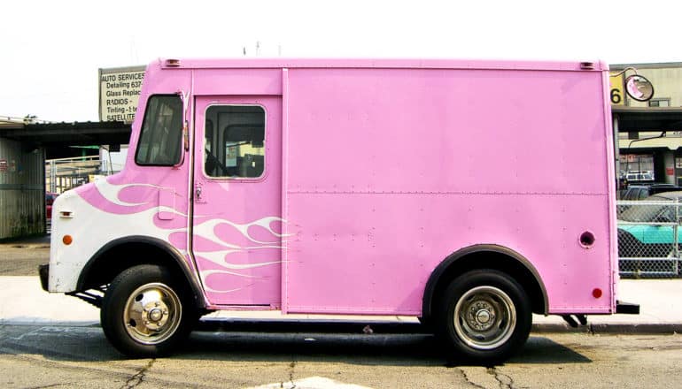 A pink delivery truck with white flames near its front parks near a curb