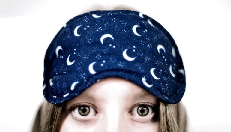 A woman wears a sleep mask on her forehead while her eyes are wide with insomnia